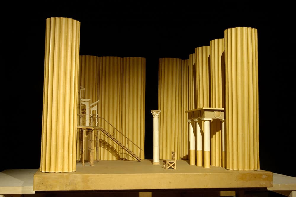 1986г. «Кориолан» В.Шекспира. Театр на Таганке. Режиссер В.Саркисов. 44х62.5х62.5см. Канелированные колонны парфеноновского диаметра (180см) образуют периптер античного храма и выполнены из тонкой компрессной бумаги по каркасу из металла, кружал из фанеры и кроличьей сетки. Внутри этого пространства еще две ордерные композиции. Одна – самого маленького ордера перестиля античного дома, другая – с помпейских фресок. В середине – скамьи и плоский бассейн. Спектакль прошел один раз, и декорации были уничтожены.